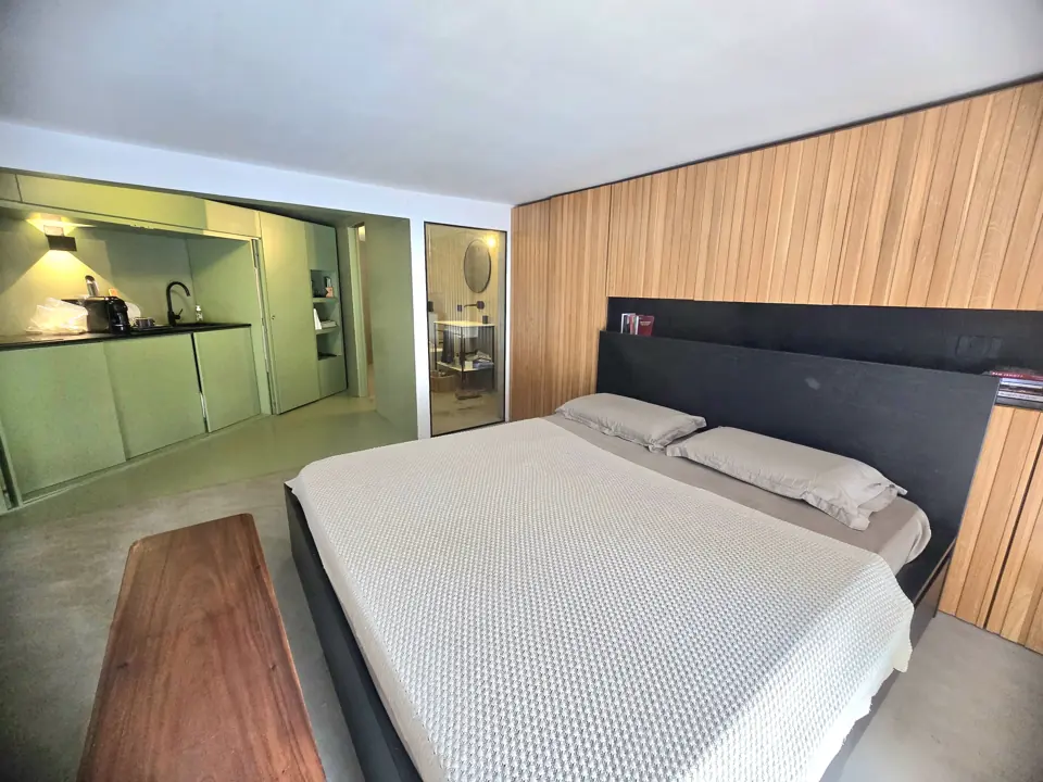 Il letto, la parete in legno e la cucina verde sullo sfondo